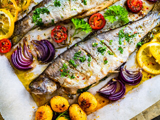 Fototapeta na wymiar Sheet pan dinner - roasted whole trouts with lemon ,rosemary, tomatoes, red onion and potatoes on cooking pan on wooden table 
