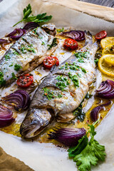 Sheet pan dinner - roasted whole trouts with lemon ,rosemary, tomatoes, red onion and potatoes on cooking pan on wooden table
