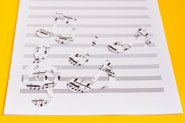 Blank sheet music and music notes cut from music text on yellow background. Copy space