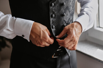 the groom fastens a button on his vest