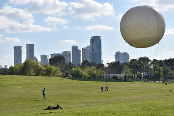 Obraz premium Tel-Aviv Park Yarkon white hot air balloon on the background of skyscrapers and green grass