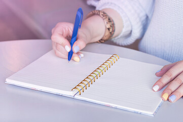 Woman writing in spiral notepad placed on desktop