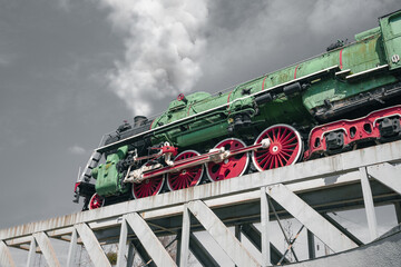 Retro steam locomotive moves along the bridge. Soviet green steam locomotive
