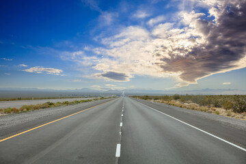 Naklejka premium Highway in countryside USA. Empty national road, passing American desert, Blue cloudy sky background
