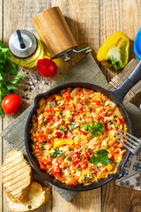 Traditional Turkish dish. Mememen (fried vegetables with scrambled egg) in a cast iron frying pan on a wooden table. Top view flat lay background.