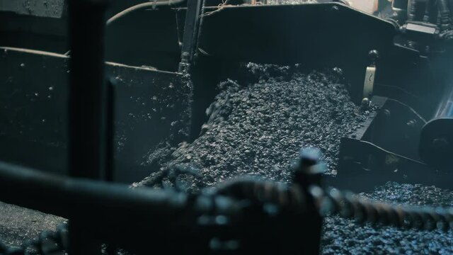 Close-up of fresh asphalt mix pouring out. An asphalt paver is laying asphalt mix on the road. Road repair, new road construction.