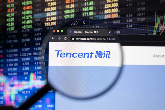 Tencent company logo on a website with blurry stock market developments in the background, seen on a computer screen through a magnifying glass