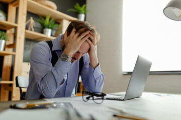 A photo of a tired architect taking off his glasses and holding his hands on his head.