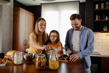 Cute little girl and her beautiful parents are smiling while cooking in kitchen at home.