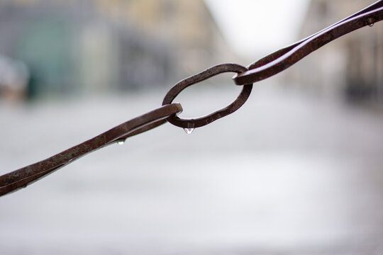 Catena isolata di metallo. La catena è antica e presenta il tipico colore ruggine del ferro forgiato a mano, non zincato. Dietro la catena, lo sfondo bokeh della Città