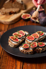 Three whole bread tapas with figs and honey on a black plate