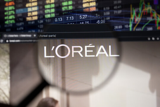 L'oreal company logo on a website with blurry stock market developments in the background, seen on a computer screen through a magnifying glass