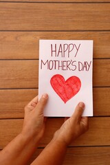 Woman's Hands holding Happy Mother's Day gift card on wooden background. Vertical. 