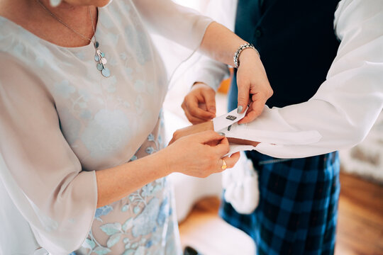 Preparing for a scottish wedding. Woman fastening cufflinks on a shirt of a man in a kilt