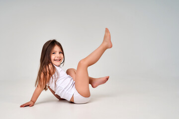 A little girl on a white background in a white T-shirt and white panties smiles