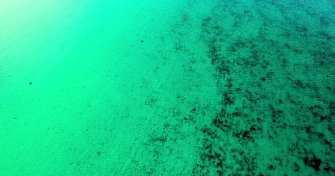 Aerial Reversing Over Shallow Turquoise Colored Water With Sunlight Reflected Off The Surface Ripples - Isle of Tiree, United Kingdom