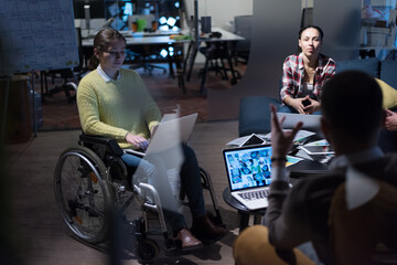 Office workers and handicaped person in a wheelchair discussing business moments in a modern office. Disability and business concept