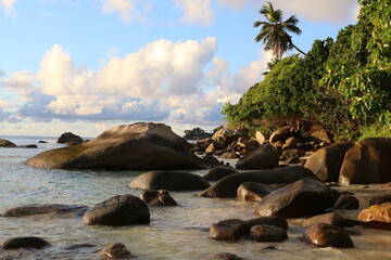 Image of a picturesque sea shore illuminated by sunlight with large smooth stones in the water with...