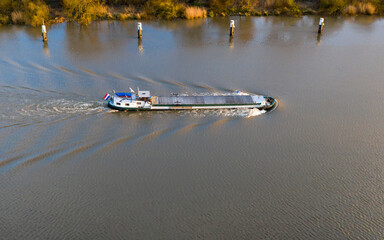 Barge navigating on the Scheldt river, near Dendermonde, Belgium. Aerial view at sunset