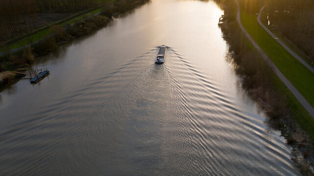 Barge navigating on the Scheldt river, near Dendermonde, Belgium. Aerial view at sunset