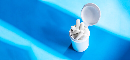 White cylindrical capsules on a matte blue background in white tube. View from above. Medical concept of treatment, prevention and side effects.