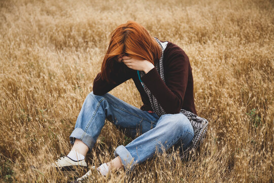 Lonely sad red-haired girl at field