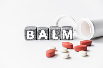 word BALM is made of stone cubes on a white background with pills. medical concept of treatment, prevention and side effects. fragrant ointment or preparation used to heal or soothe skin