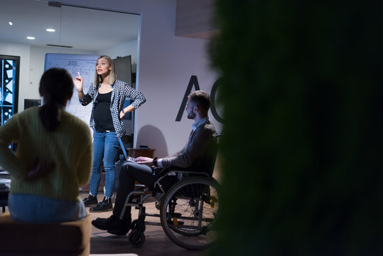 Office workers and handicaped person in a wheelchair discussing business moments in a modern office. Disability and business concept