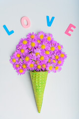 Waffle cone with alpine aster flowers on a blue background. The concept of March 8, flowers for your beloved. The text is Love. Flat lay, top view.