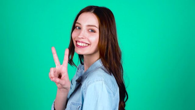 I'm great. Cheerful joyful young white girl, with long hair and blue eyes, wears youth clothes, turns to the camera and shows the sign of peace with her hands.
