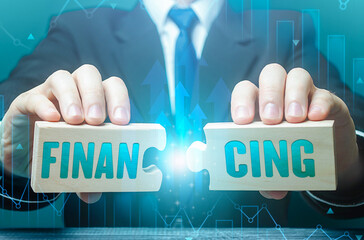 Businessman connects puzzles with the word financing. Investing in a business project, raising funds. Credit, donations, taxes, support grants, savings and subsidies. Financing from the budget.