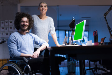 Man in wheelchair and his is female colleague working in the modern co-working office