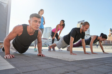 Fototapeta na wymiar Young mixed race athletes doing push ups on city square