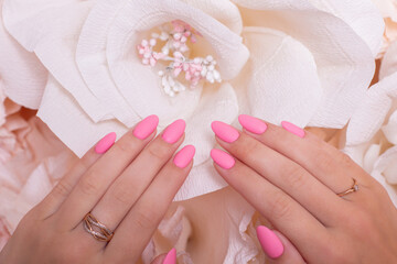 Fototapeta premium Female hands with wedding manicure nails, pink gel polish, on paper flowers background