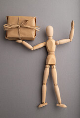 Wooden mannequin holding a gift box on gray pastel background. close up.