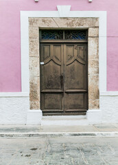 Close up of large brown wooden door with stone door trim on a pink and white stucco Spanish colonial house, Campeche, Mexico.