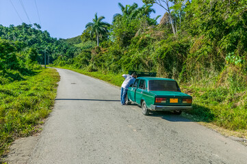 Fototapeta na wymiar Cuban man with car trouble raising the hood of his car on a lonely deserted road in the Escambray Mountains in Cienfuegos, Cuba.