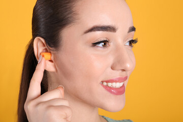 Obraz na płótnie Canvas Young woman inserting foam ear plug on yellow background, closeup