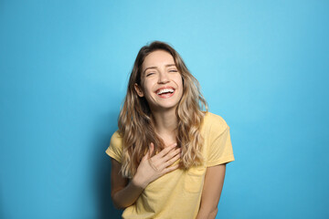 Fototapeta premium Cheerful young woman laughing on light blue background