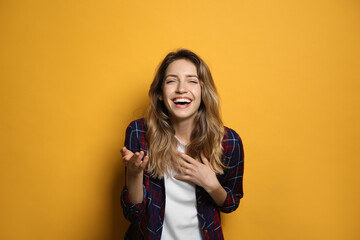 Cheerful young woman laughing on yellow background