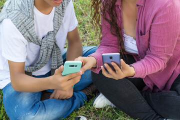 Pareja de jóvenes amigos colombianos mirando el teléfono móvil sentados en el césped