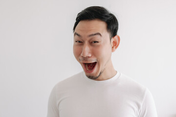 Funny grin smile face of Asian man in white t-shirt isolated on white wall.