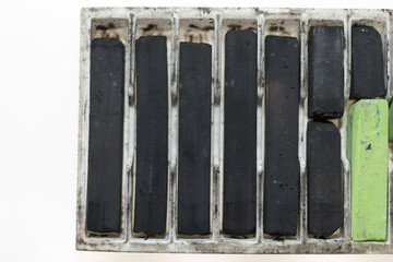 slightly used black artist pastel chalks (or chalk pastels) in a white tray on a white ground