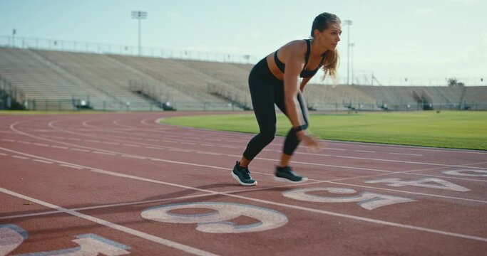 Attractive young woman sprinting down the track at the stadium, epic running workout, fitness lifestyle