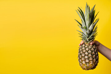 Hand of unknown woman holding pineapple - female hold fresh fruit on bright yellow background - healthy eating and diet modern concept