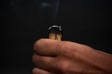 Hand holding palo santo burning with beautiful aromatic smoke, holy sacred tree stick.