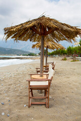 Empty beach with old parasol and beach wooden chairs located in Crete during a cloudy day. Greece.