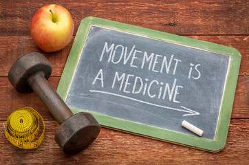 movement is a medicine - white chalk text on a slate blackboard sign against weathered wood with a dumbbell, apple and tape measure, fitness and healthy lifestyle concept