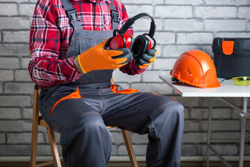Builder puts on personal protective equipment. Manual worker putting protective headphones. - obrazy, fototapety, plakaty