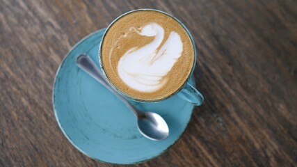 A hand picking up a mug of plant based coffee latte from the wooden table with a latte art swan on it